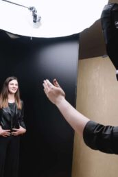 A behind the scenes photoshoot of a London portrait photographer smiling and directing a woman in a leather jacket