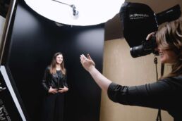 A behind the scenes photoshoot of a London portrait photographer smiling and directing a woman in a leather jacket