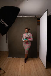 A behind the scenes London photoshoot of a black woman in a pink and green dress and studio lights