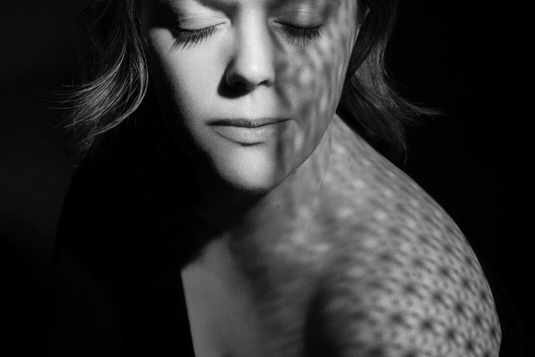 A woman with closed eyes looking over her shoulder with creative light from a London boudoir photography photoshoot