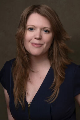 An image of a female photographer in London with a brown background and blue dress
