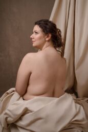 A woman with curly hair sitting in a canvas looking over her shoulder on a London boudoir photography photoshoot