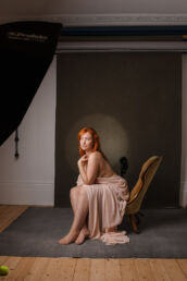A woman with red hair sitting on a chair in a photostudio at a London portrait photographer session