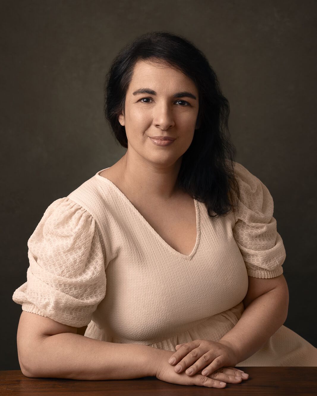 a female in a cream dress with warm vintage tones sitting at a wooden desk for a female portraits photography session