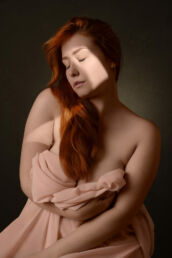 A woman with red hair clutching a pink cloth on London boudoir photography photoshoot