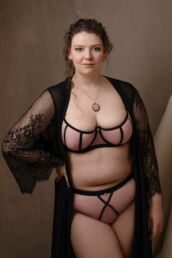 A curvy woman in pink lingerie and black robe on a boudoir photography london photoshoot
