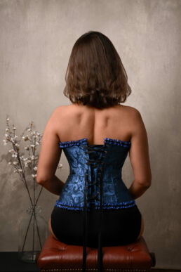 an asian woman on a boudoir photoshoot in a royal blue corset with her back the camera and flowers.
