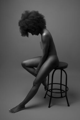 a black woman on a stool looking down on a black and white boudoir photoshoot