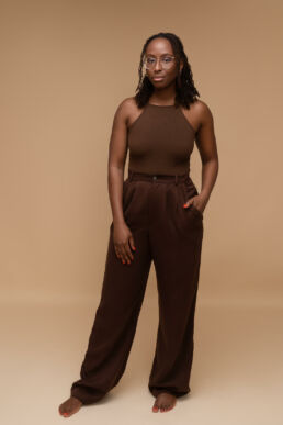 a black woman in brown trousers and brown top with glasses on a beige background from a london headshot photography photoshoot