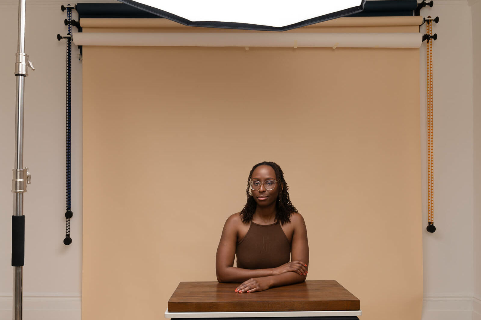 a black woman in a brown top sitting at an oak desk with beige background on a london studio photography photoshoot
