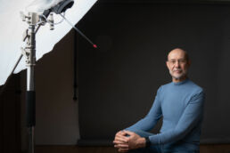 A man in glasses and a blue shirt sitting for a london studio photography photoshoot