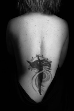a womans back with freckles and tattoo in a tasteful nude photo
