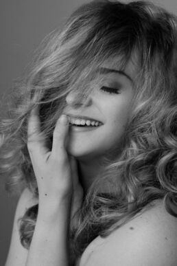 A woman smiling with her hand to her lips showing boudoir makeup looks on a London boudoir photoshoot