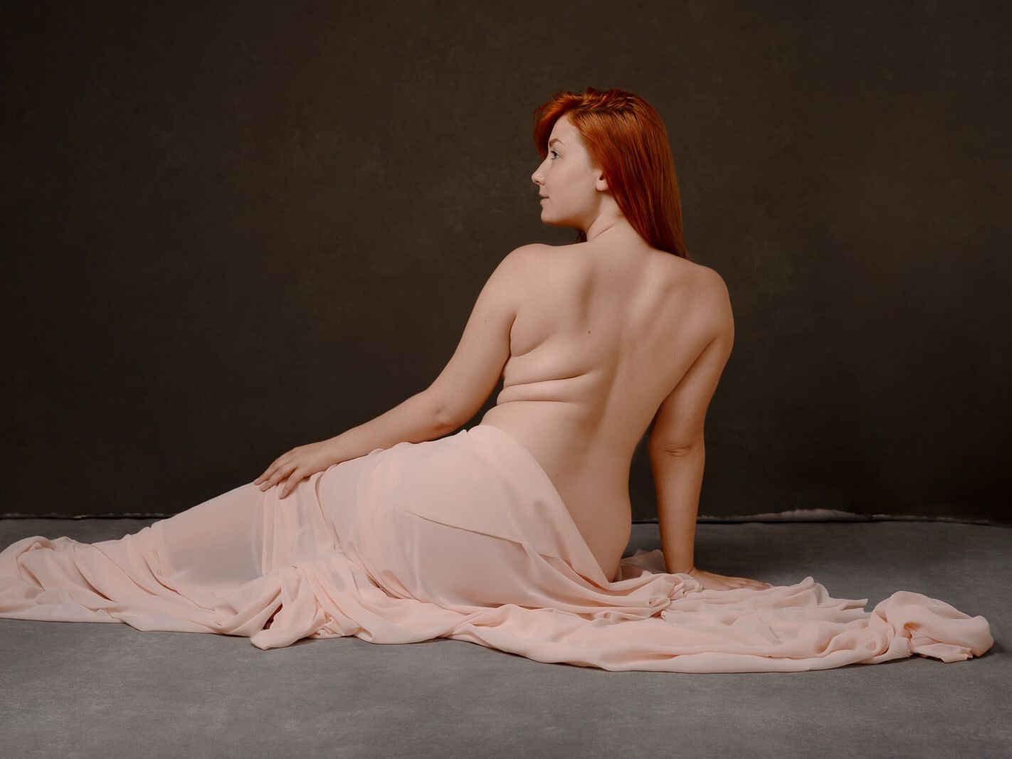 a woman lying down with red hair wrapped in silk on a plus size boudoir photographer photoshoot