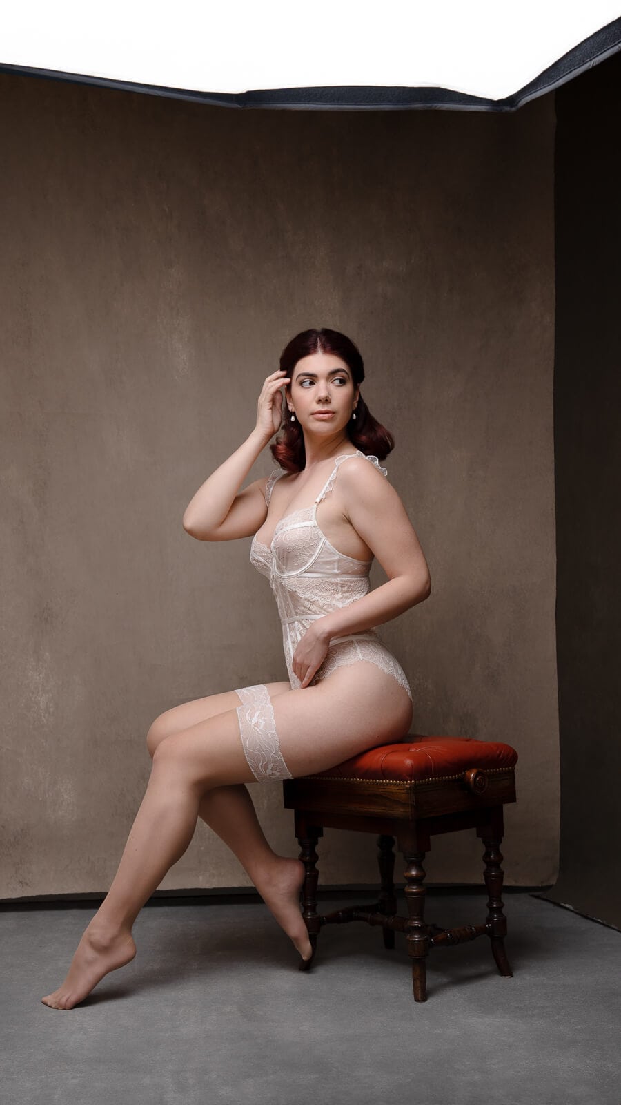 Behind the scenes of a boudoir photoshoot with a woman in lingerie seated under studio lighting.