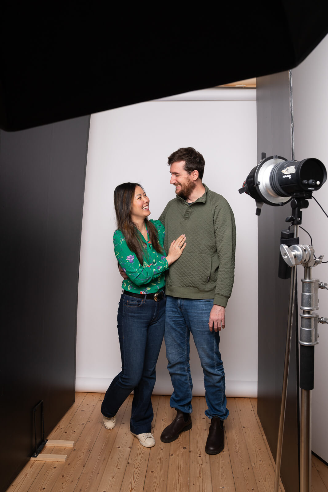 Couple embracing and smiling during a headshot photoshoot, surrounded by studio equipment.