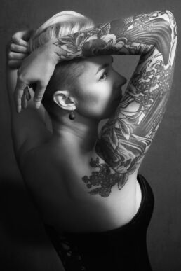 a woman with bird tattoos arching backwars in a corset on a boudoir photoshoot in London
