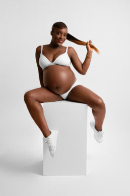 a black woman on a maternity photography photoshoot sititng on a cube in white underwear