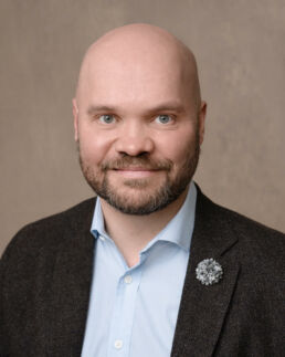 A bald man in a suit with a blue shirt and brooch on a london headshot photography studio photoshoot.