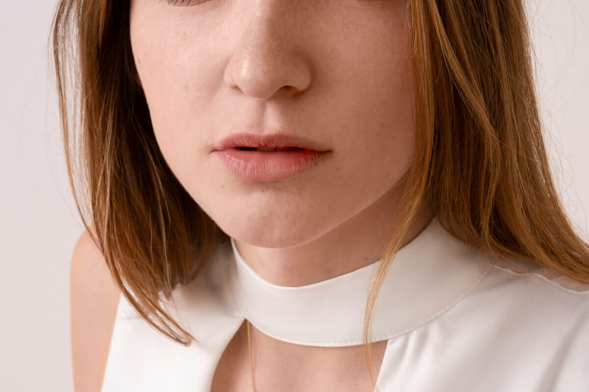 A woman with auburn hair and brown eyes looking into the camera with a white top on a london headshot photoshoot. the side light is an example how to take good headshots