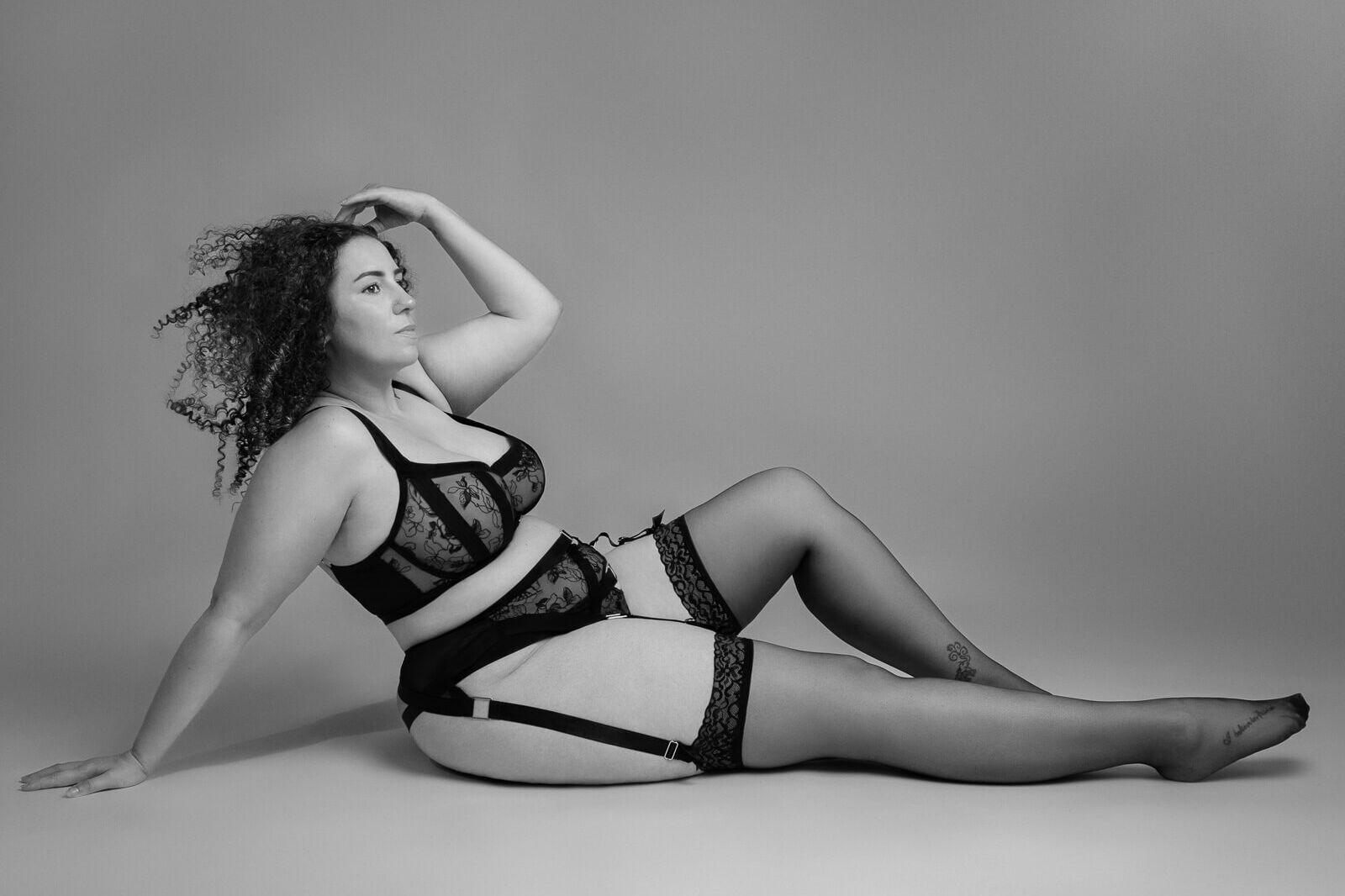 Curvy woman lying on the floor with full lingerie set and stockings in black and white on a boudoir photography uk photoshoot