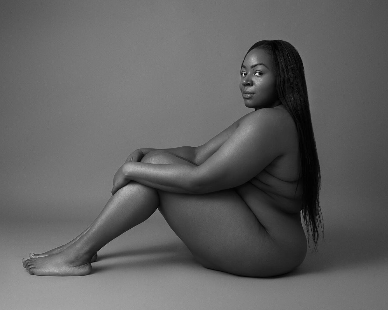 a black woman with long hair on the floor with knees up in a black and white boudoir photography photoshoot