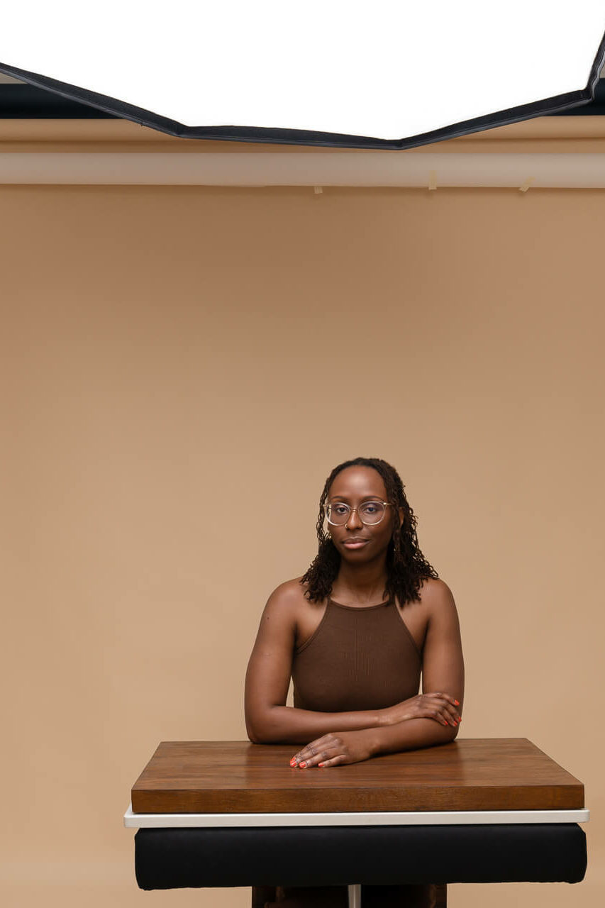 a black woman sitting at a posing desk surrounded by photography equipment in brown hues and taken by a london headshot photographer