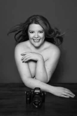 female london photographer with a camera sitting at a wooden desk with hair blown by fan with camera