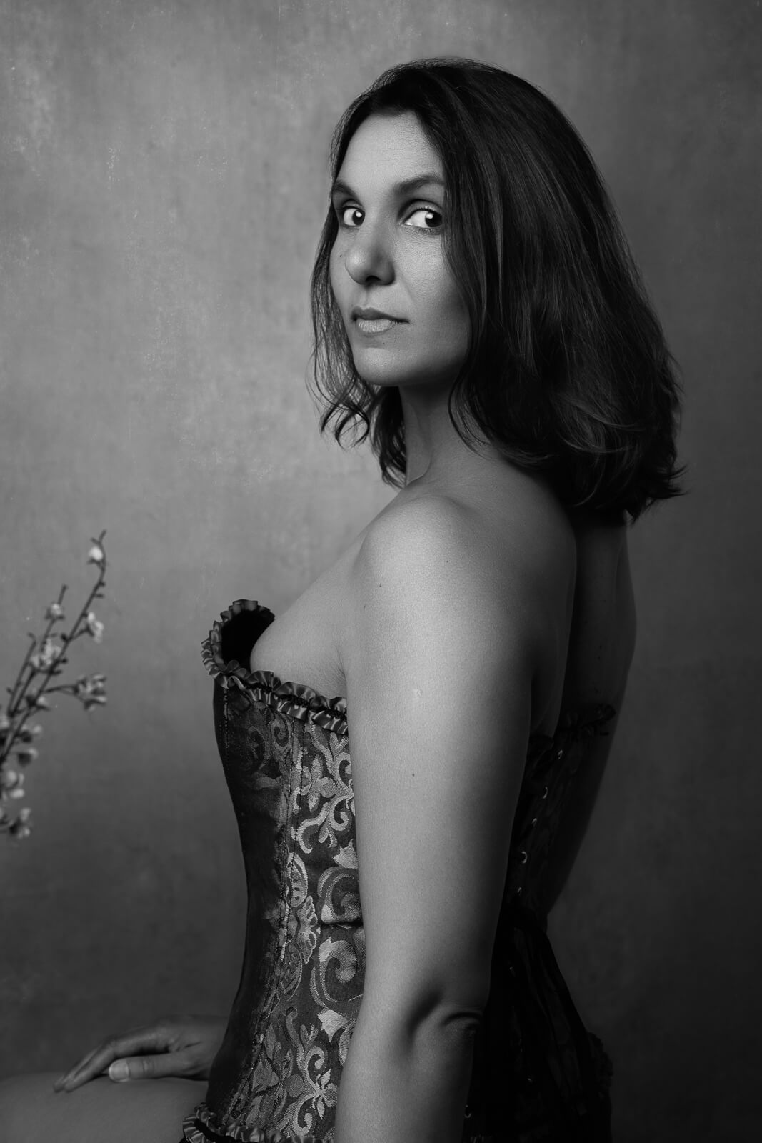 a south asian woman in a corset looking over her shoulder with flowers on a boudoir photoshoot for mums uk