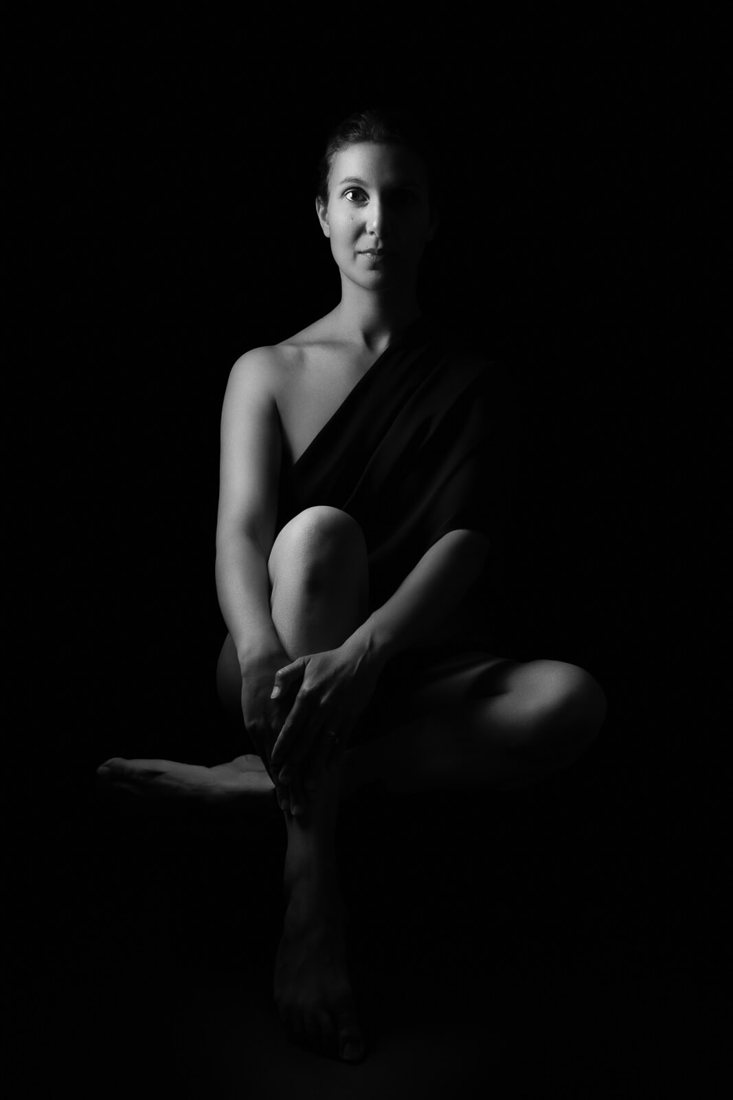 a south asian woman in dark shadow light holding her leg on a boudoir photoshoot for mums uk