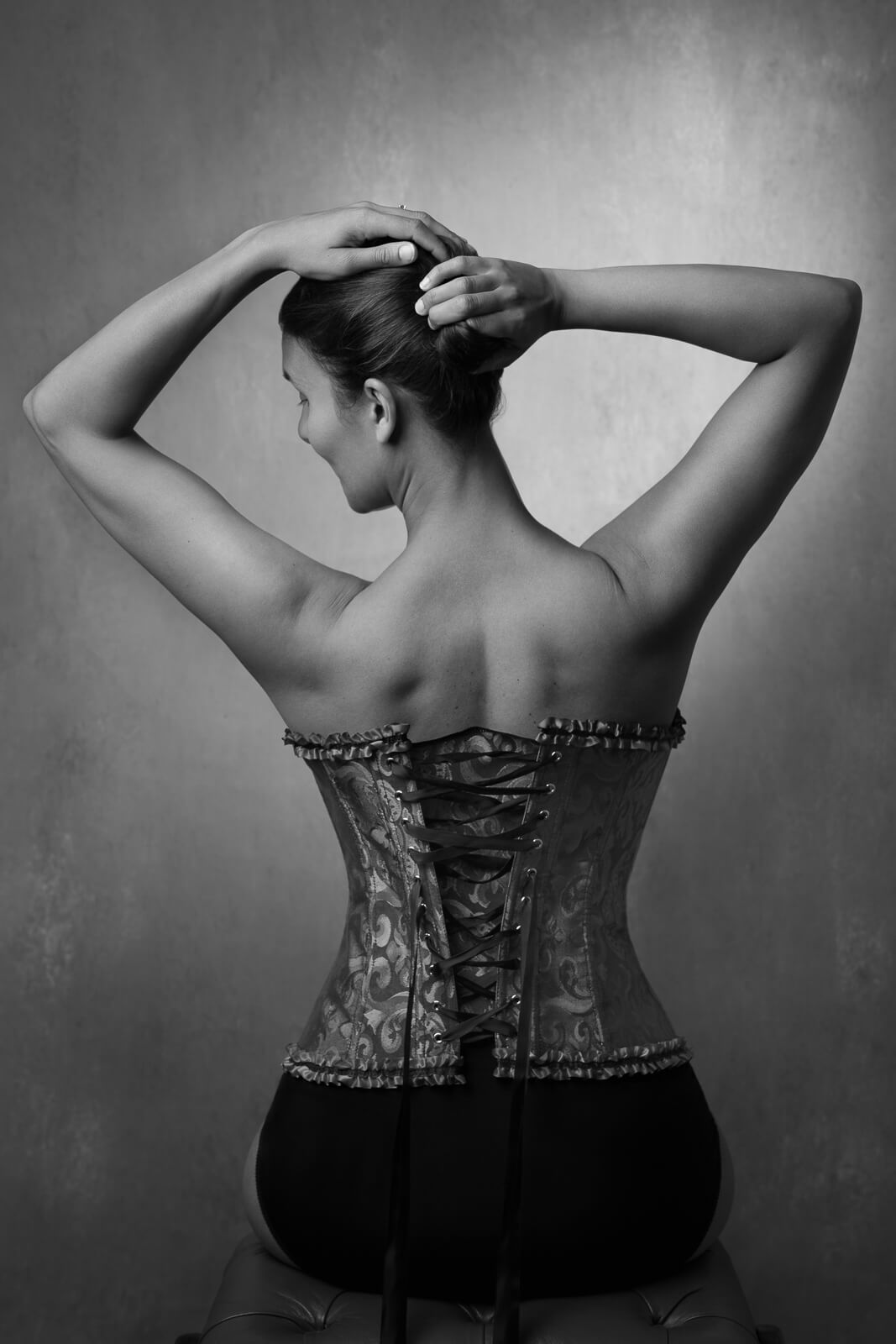 a south asian woman in a corset playing with her hair and seated on a boudoir photoshoot for mums uk