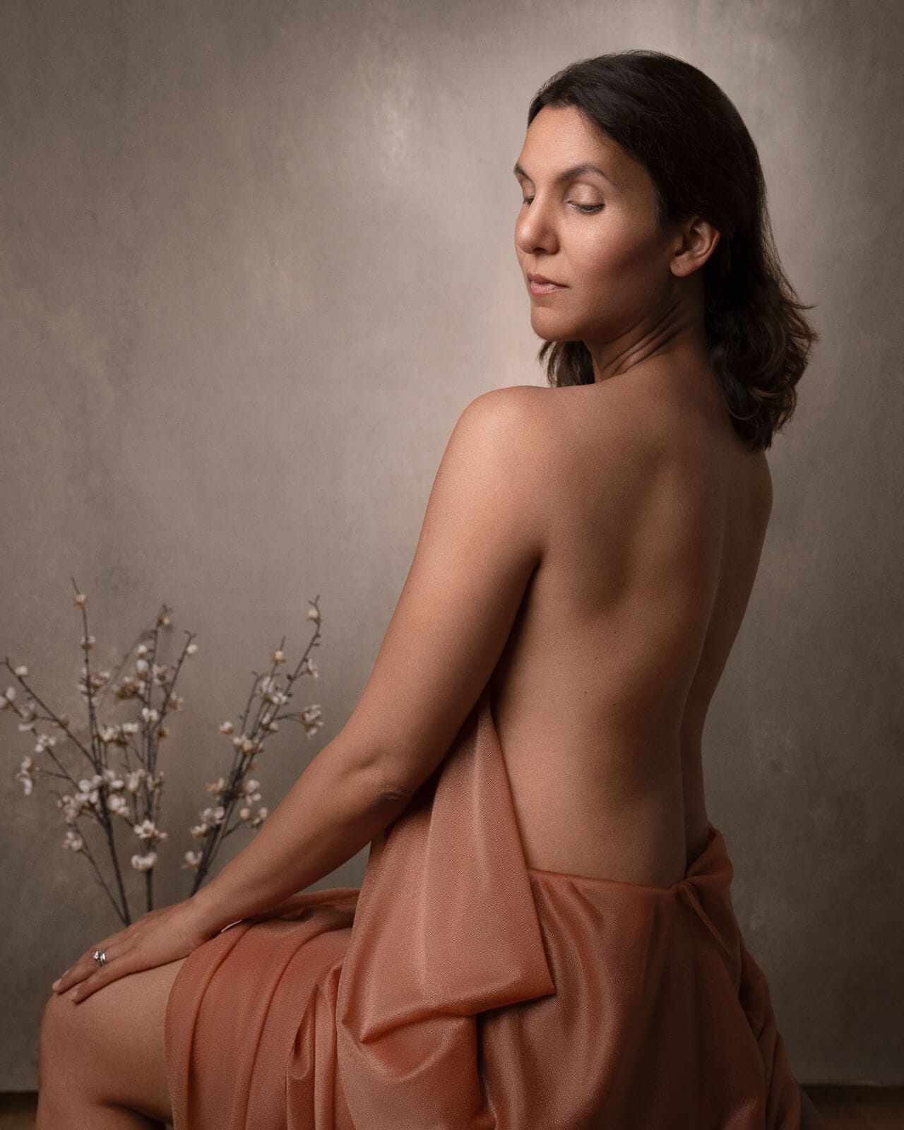 a south asian woman looking ove her shoulder in orange drapery with flowers on a boudoir photoshoot for mums uk