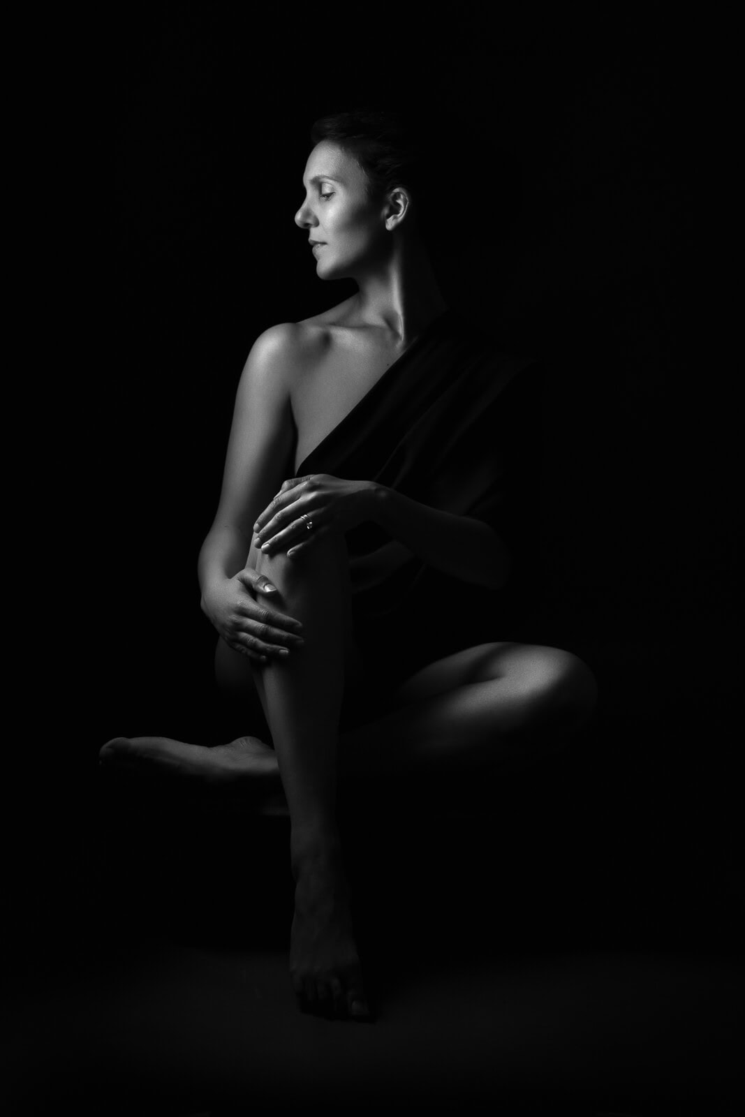 a south asian woman looking to the side seated in dark shadow in black and white on a boudoir photoshoot for mums uk