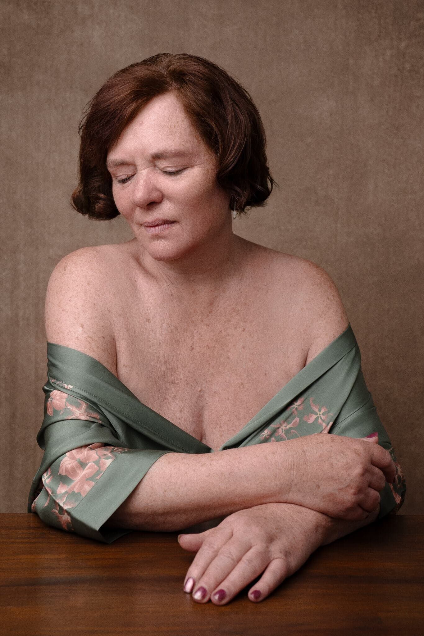 Boudoir Photography for Mature Women in a green robe and red gold tones seated looking away