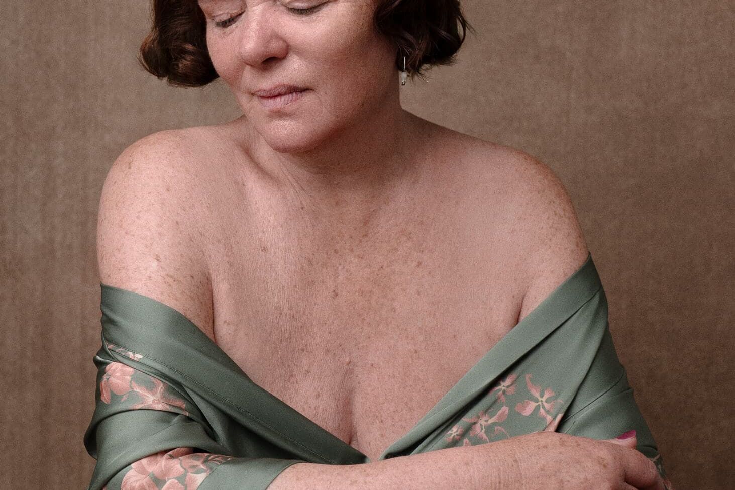 Boudoir Photography for Mature Women in a green robe and red gold tones seated looking away