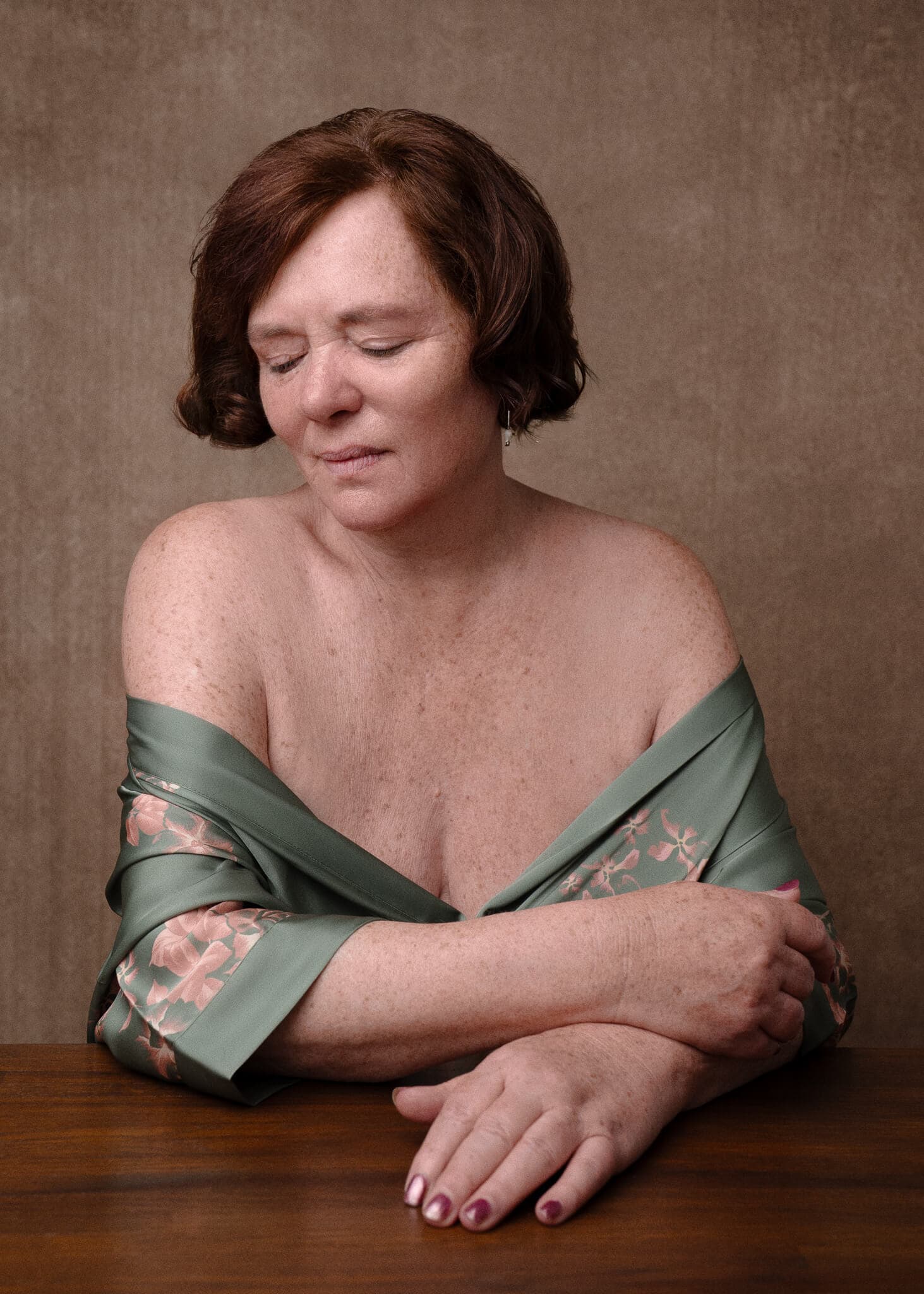Boudoir Photography for Mature Women in a green robe and red gold tones seated looking away