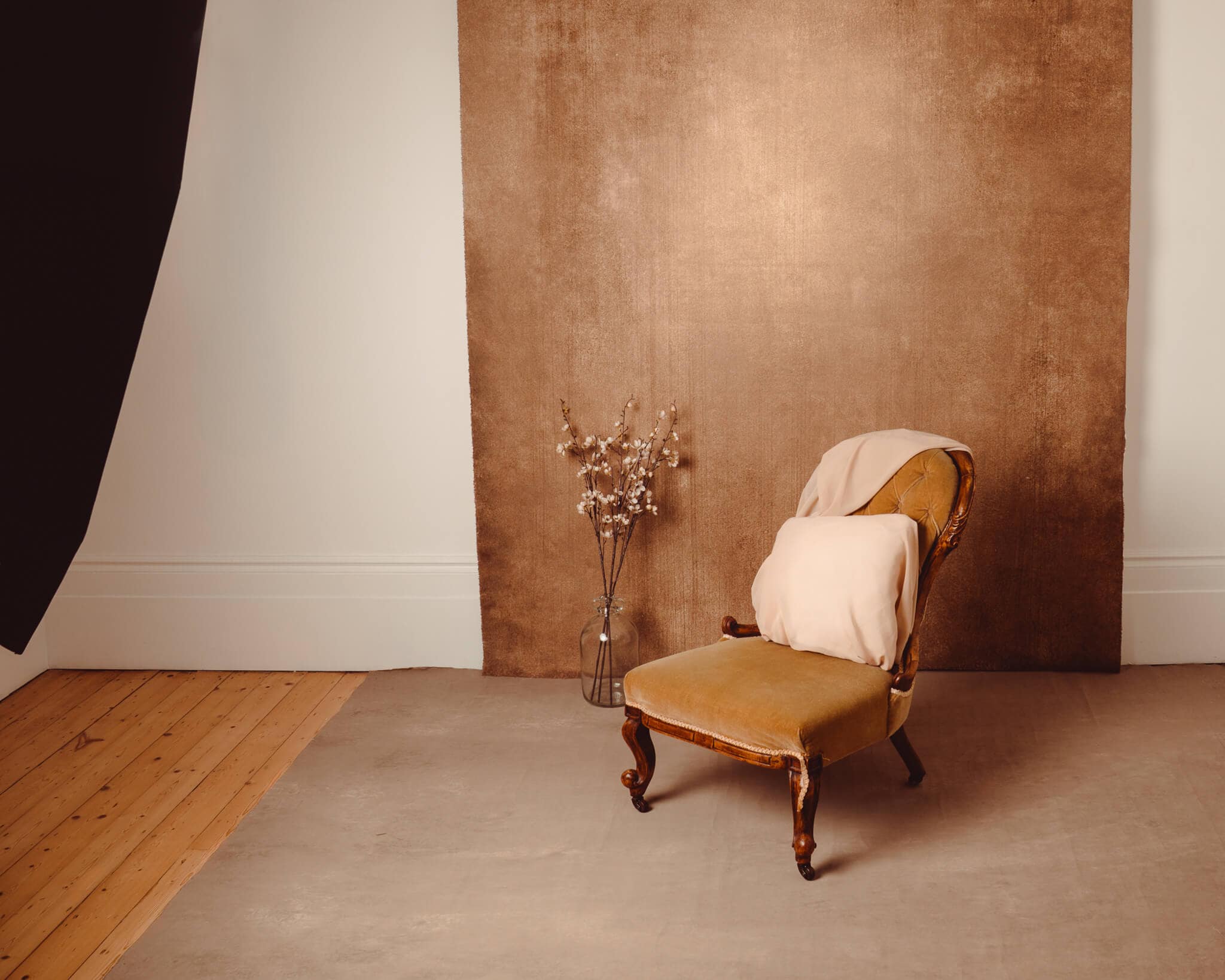 Private London boudoir studio with a vintage chair, textured backdrop, flowers and wooden floors.