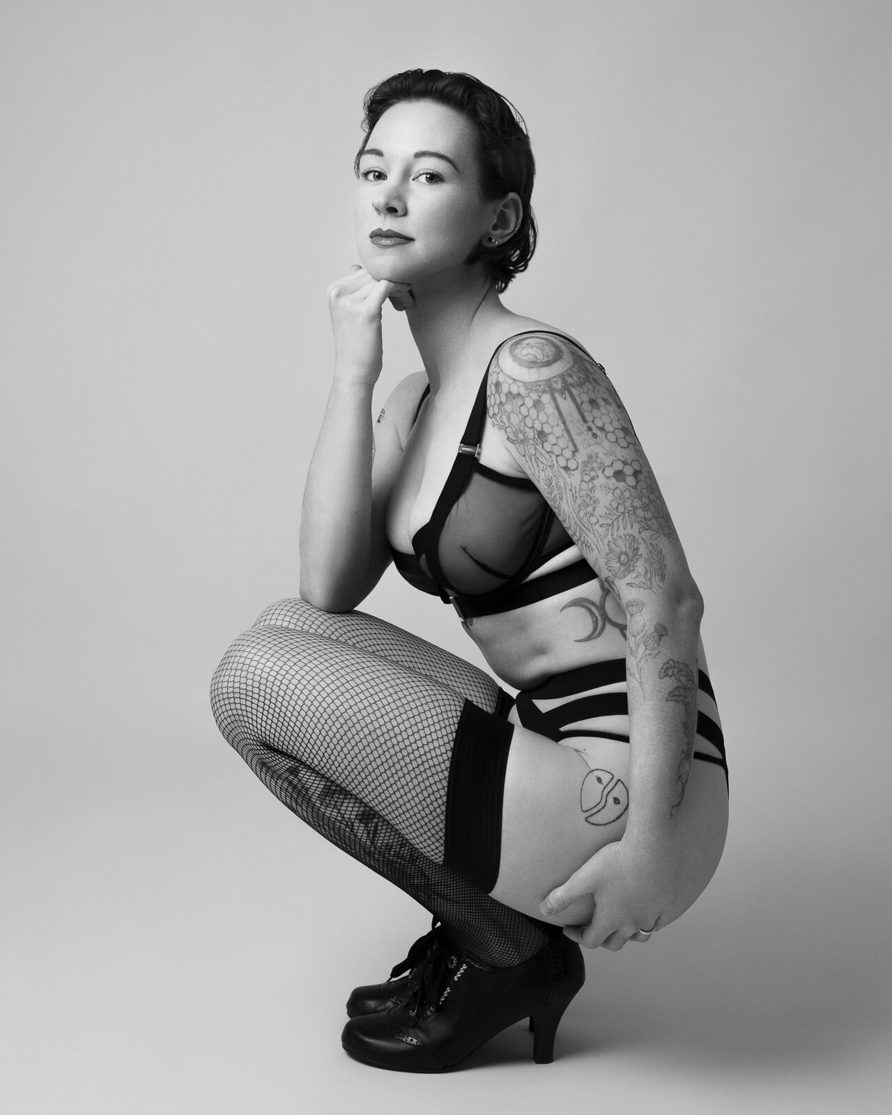 a woman crouching in heels and lingerie with her hand to her chin on a london boudoir session