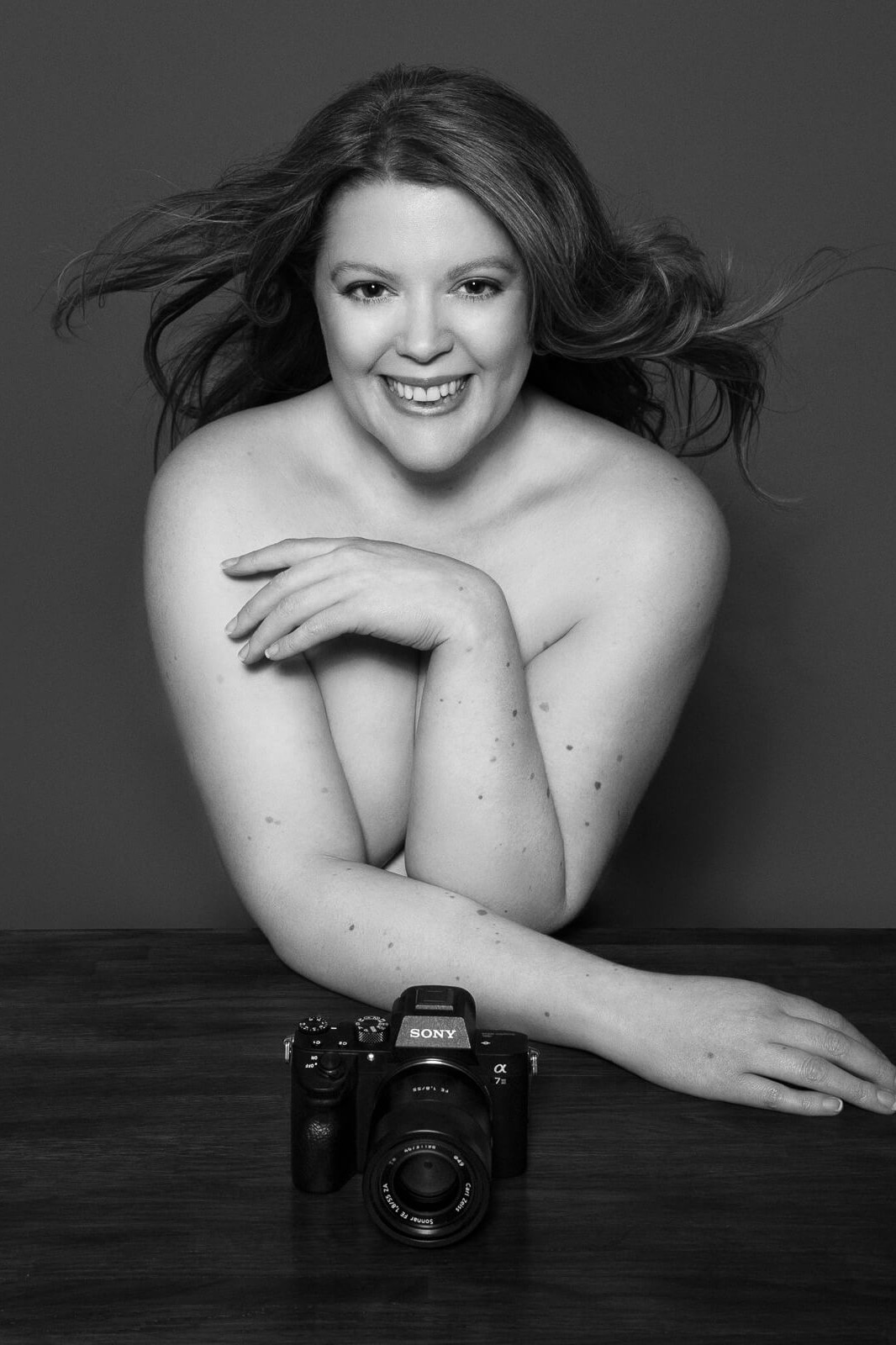 Siorna in her London portrait studio, seated at a wooden table with camera in hand.
