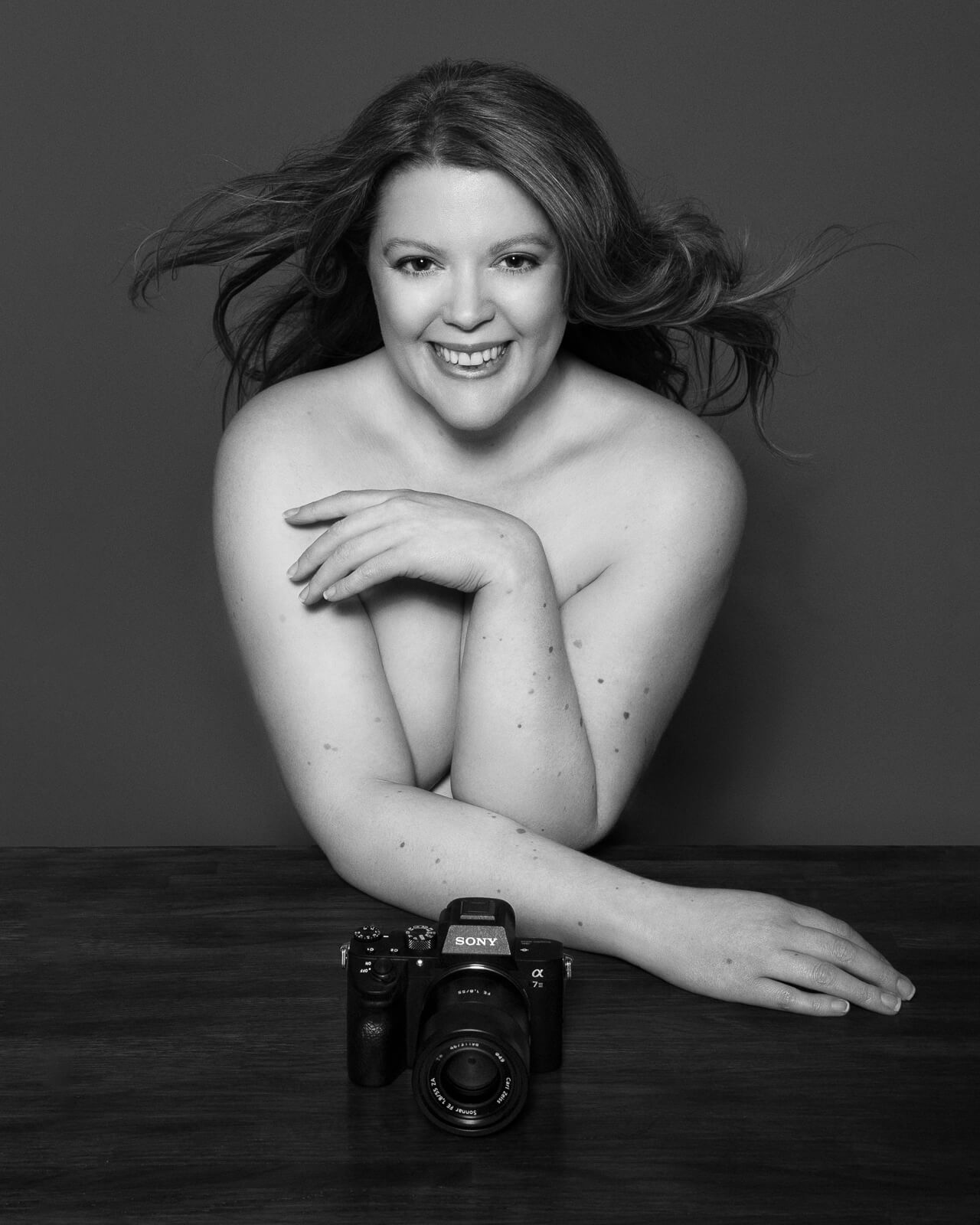 Siorna in her London portrait studio, seated at a wooden table with camera in hand.