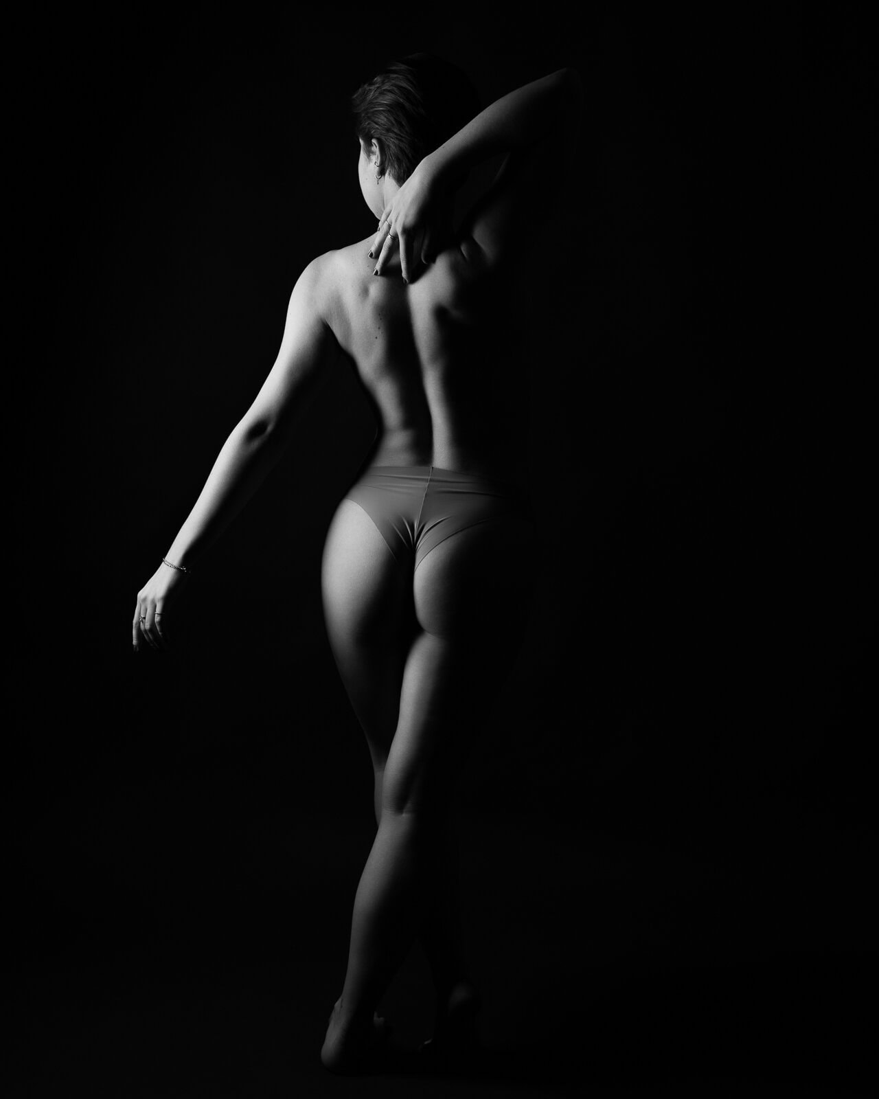 a woman's back and legs on a dark and sultry boudoir photoshoot in London with light and shadow