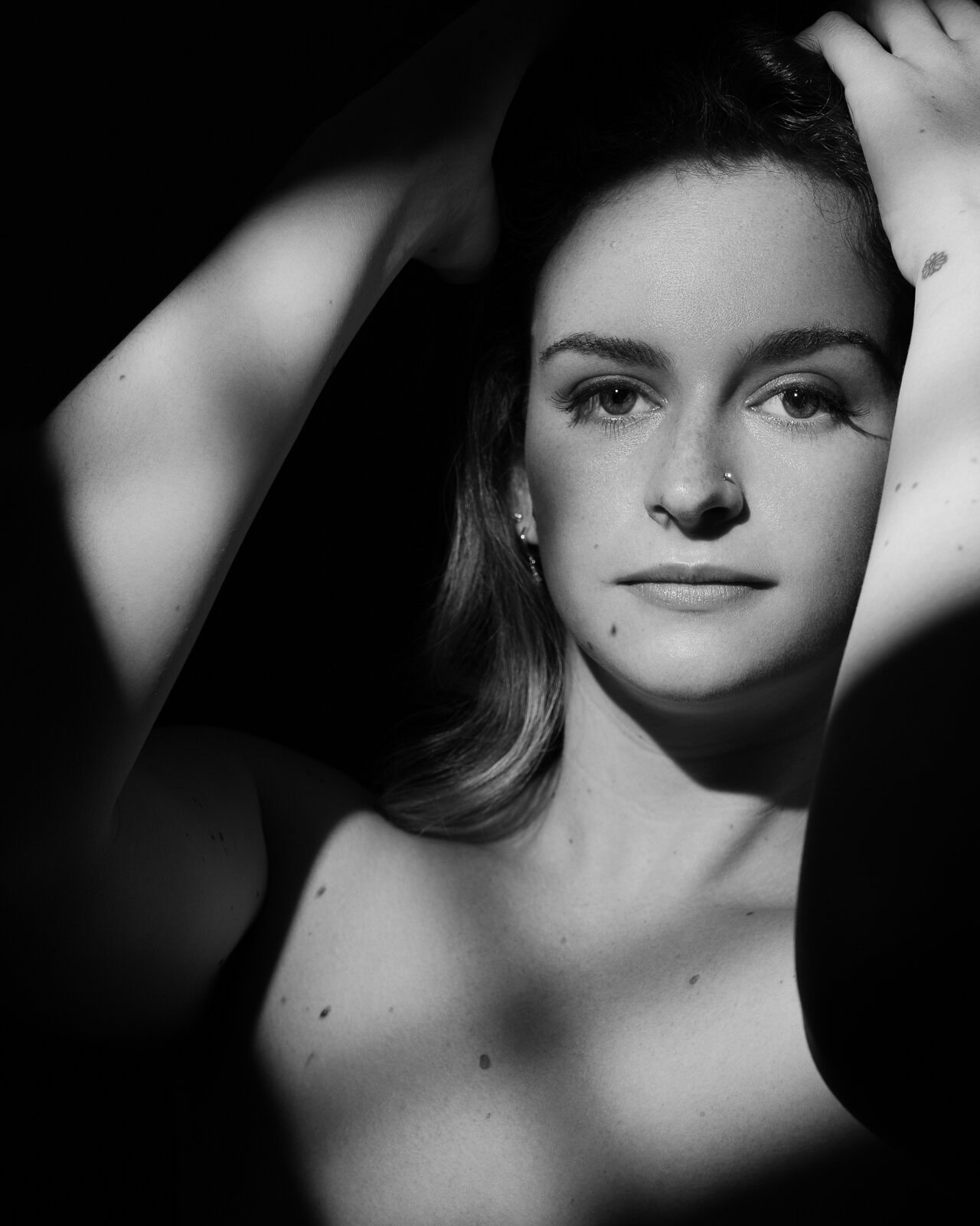 a womans' face in window light in a dark and sultry boudoir photography style with shadow and light