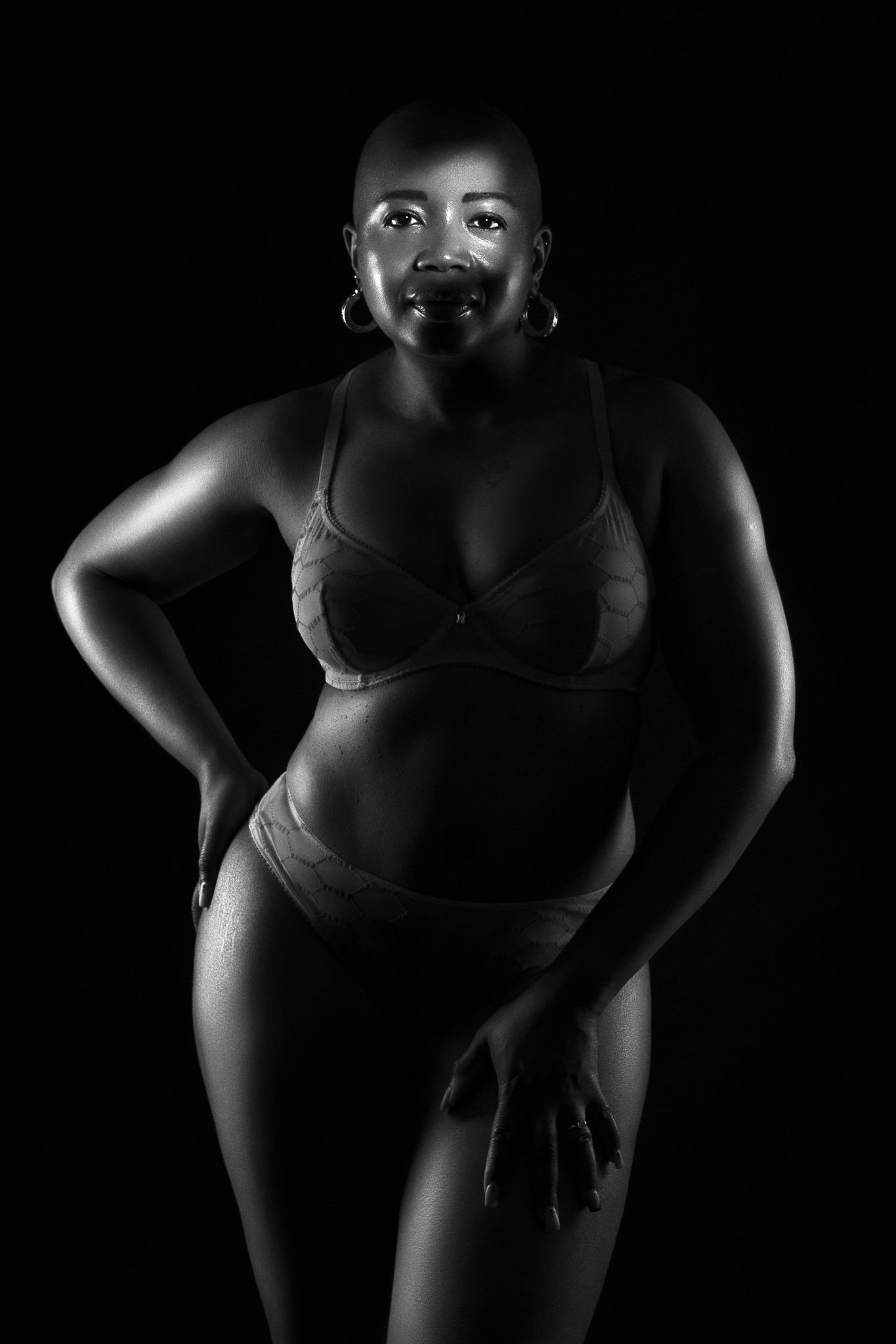 Black curvy woman in lingerie, lit dramatically with light tracing her body and a strip of light across her eyes. Classic boudoir portrait.