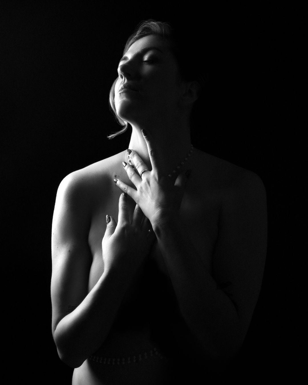 Black and white high-contrast silhouette of a woman holding her neck in a contemplative pose, expressing the female gaze in boudoir photography.