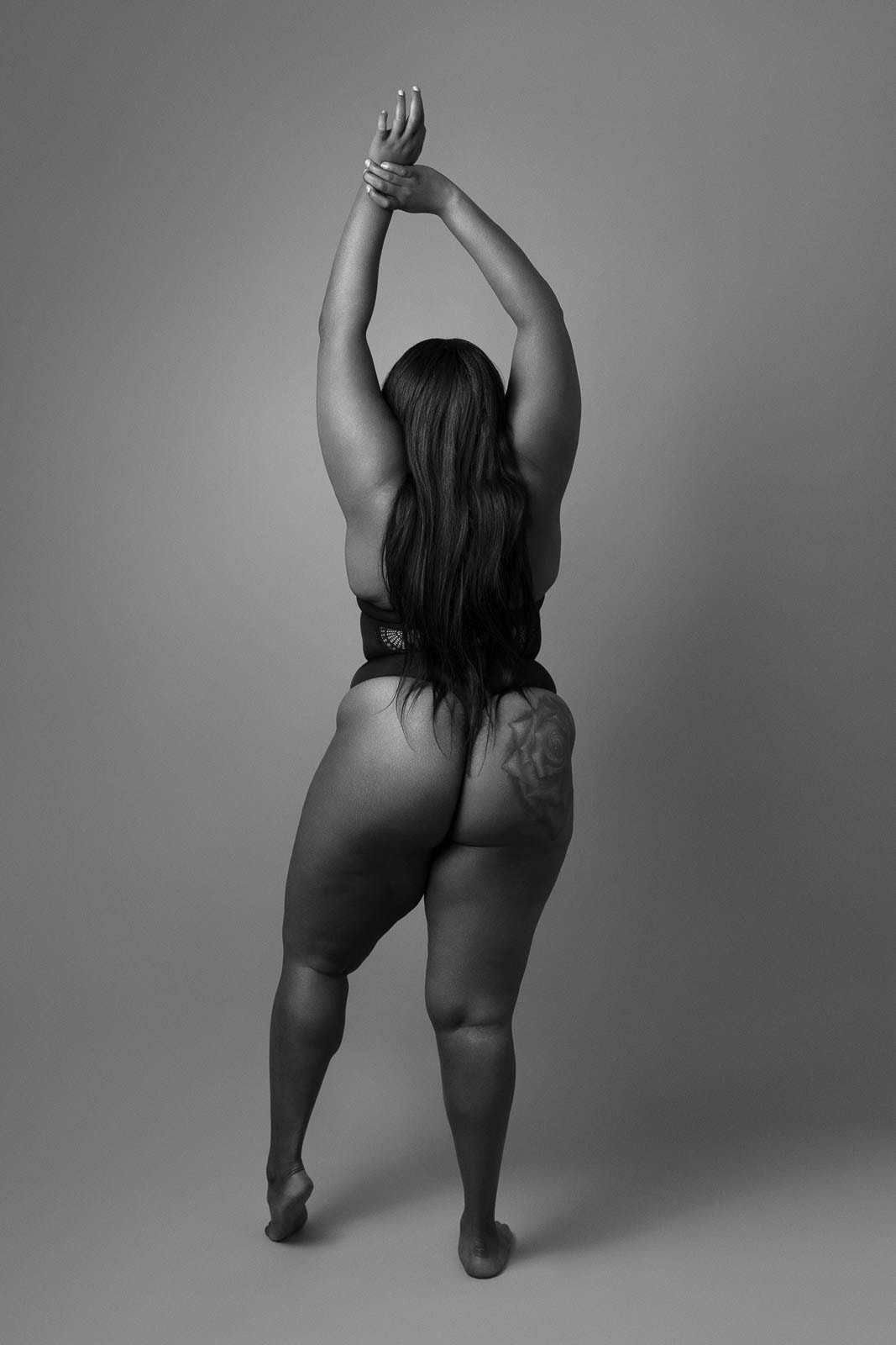 Black and white fine art nude photograph of a woman standing with her back to the camera, arms raised and one foot lifted, expressing freedom and authorship. Exhibited at the Art Icon ‘Sex and Politics’ show in Paris