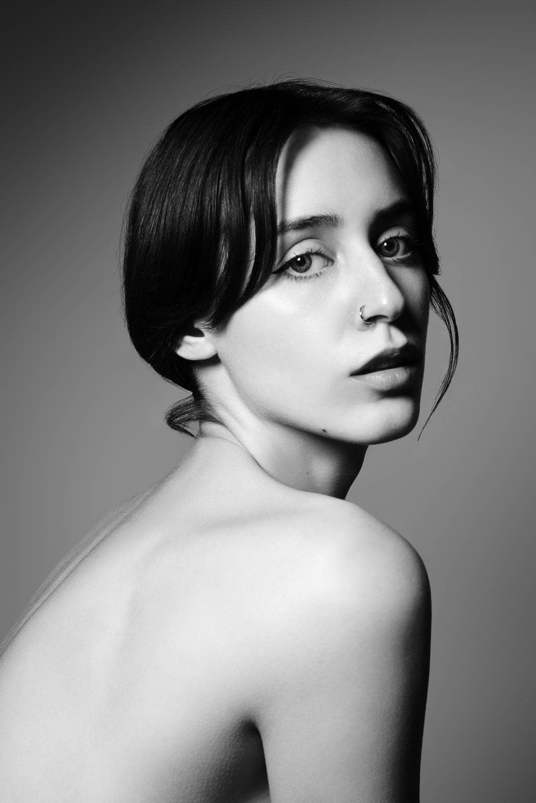 Black and white close portrait of a person with bare shoulders looking towards the camera during a boudoir photoshoot.