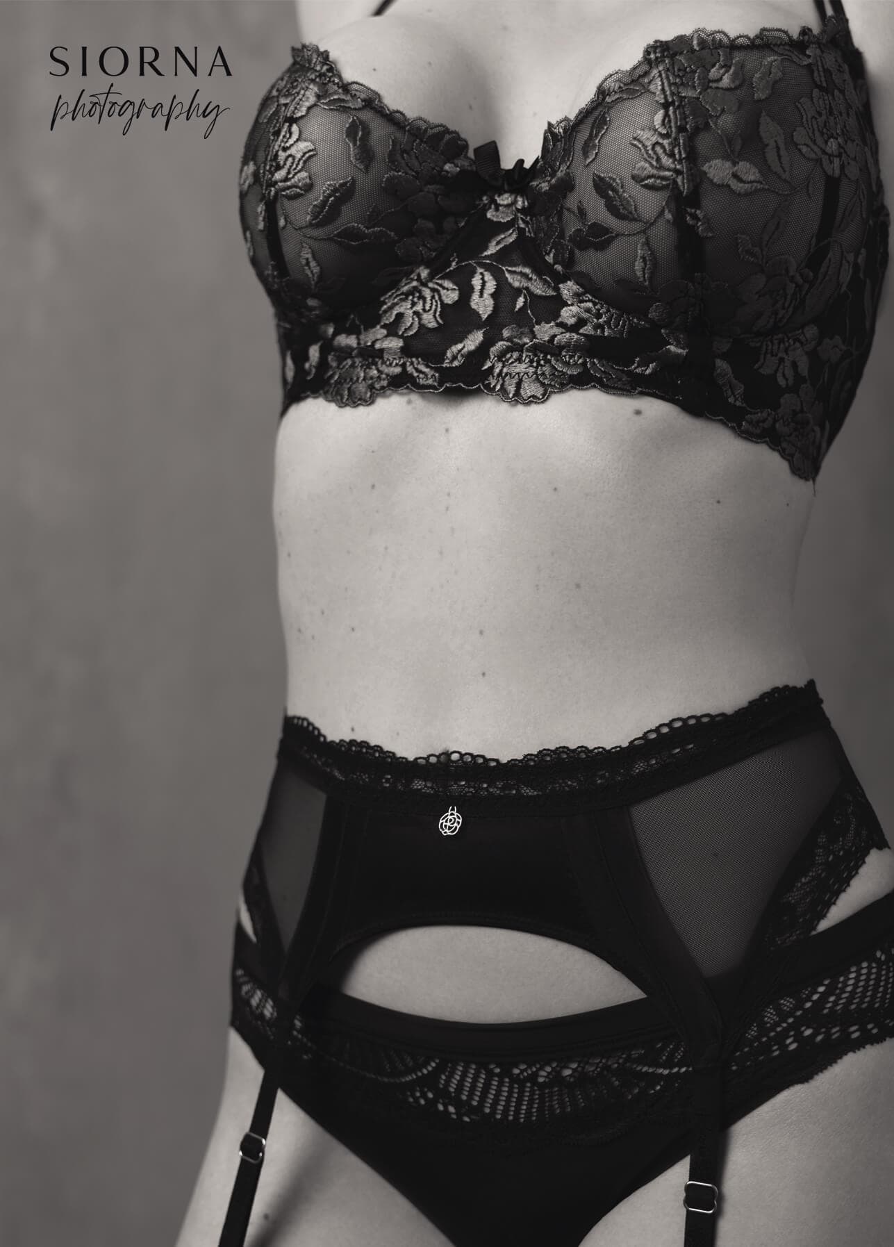 Black and white boudoir portrait showing a woman’s torso in black lace lingerie