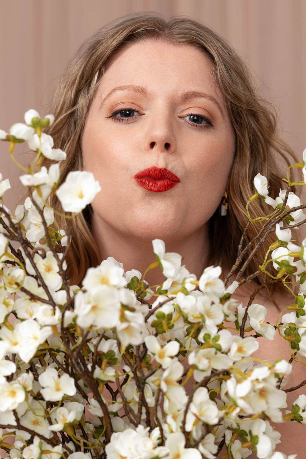 Siorna Ashby, London boudoir photographer, smiling and blowing a kiss amongst white flowers